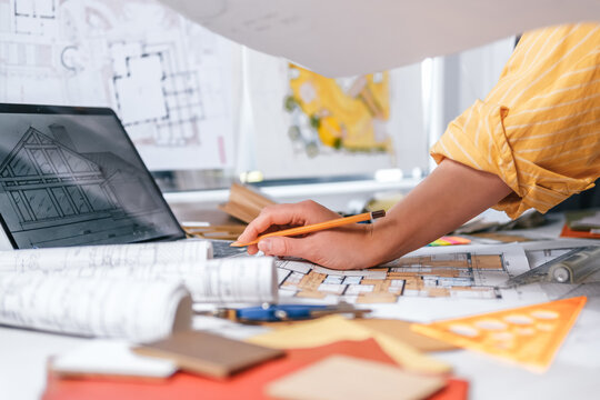Interior design process with hands selecting wood sample over architectural plans, floor plan, laptop and color palette, residential renovation planning and material selection concept.