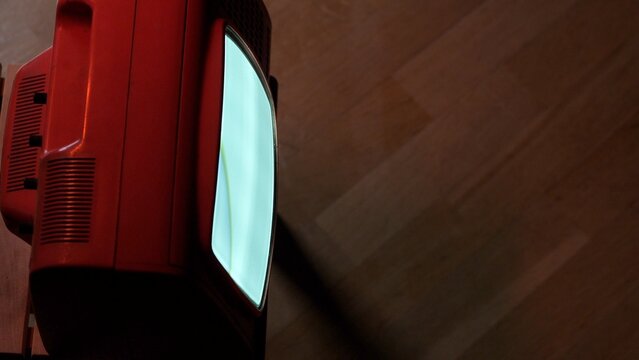 Red retro cathode ray tube television with a bright glowing screen illuminating the dark room, representing nostalgia, vintage technology, and media entertainment from past decades