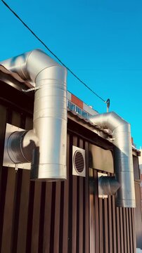 Metal ventilation ducts on corrugated wall under clear blue sky, outdoor exhaust pipes mounted to workshop exterior, steel elbow