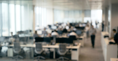 Fototapeta premium A blurred view of a modern office space filled with employees working at their desks. The bright interiors emphasize a dynamic work environment.