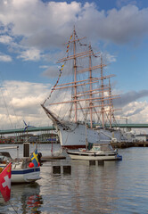 Fototapeta premium Tall ship moored in Gothenburg harbor with waterfront skyline, marina boats and dramatic evening clouds in Sweden.