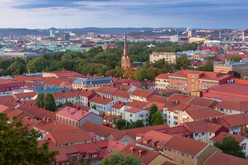 Obraz premium View of illuminated church spire rising above Gothenburg rooftops and green parkland at dusk in Sweden.