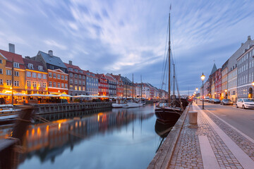 Quiet Nyhavn waterfront at dawn with moored boats, calm canal reflections, and soft early morning light in Copenhagen, Denmark. © Kavalenkava