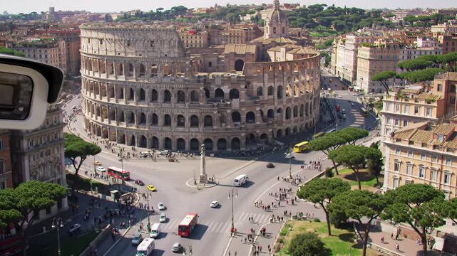A high-angle close-up of a static, white dome CCTV security camera overlooking a sun-drenched Rome cityscape with the Colosseum and busy street panning left. Modern surveillance concept