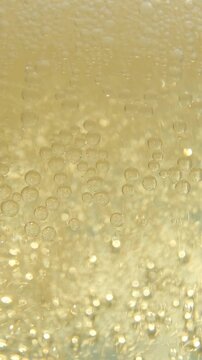 The highly carbonated golden drink flows. Dense microbubbles quickly form and move upward, creating a dynamic effervescent motion and vibrant texture in close-up macro photography.