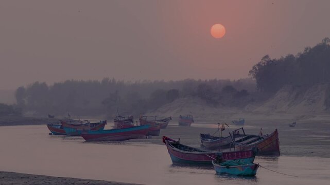 Colorful fishing boats anchored on a calm river beach at sunset with misty shoreline