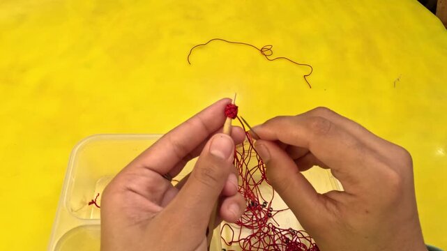Close-up of Moroccan artisan making Aqad knots by hand using a hook tool. Traditional textile technique creating decorative buttons for caftans and djellabas, showcasing craftsmanship.