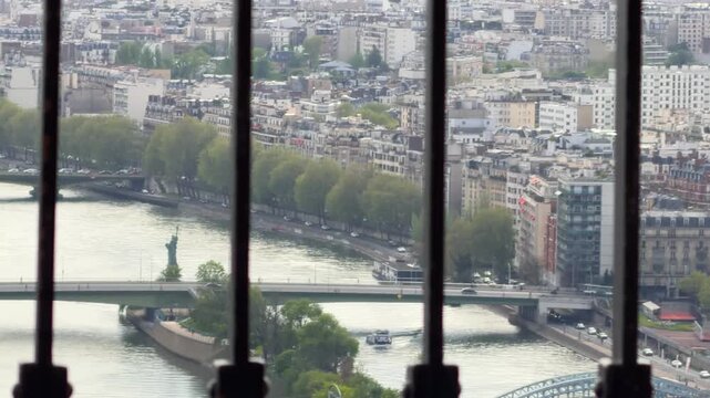 Paris skyline showing the Seine River, city buildings, bridges, and the Statue of Liberty, viewed through a protective railing from the Eiffel Tower