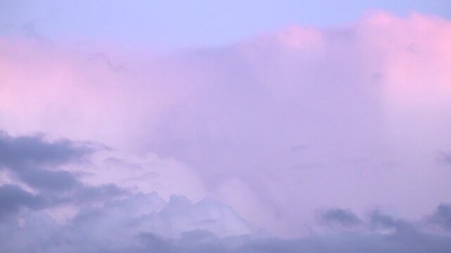 A time lapse of billowing purple and pink Cumulous Nimbus and Cirrus clouds are pushed across the sky by the wind at sunset.