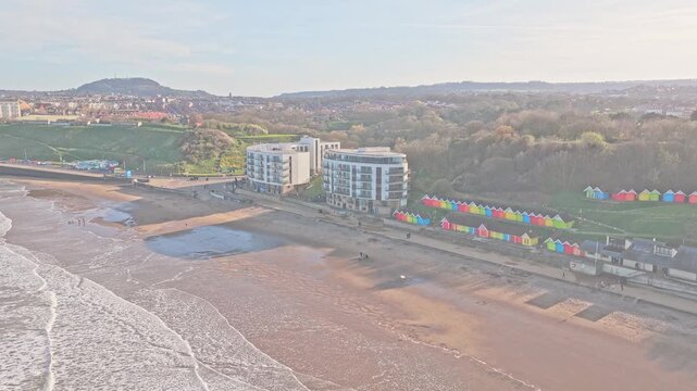 Sands Sea Front Apartments on Peasholm Gap North Bay Scarborough North Yorkshire England United Kingdom stand beside beach huts and promenade above tidal shoreline, aerial drone slow forward flight sh