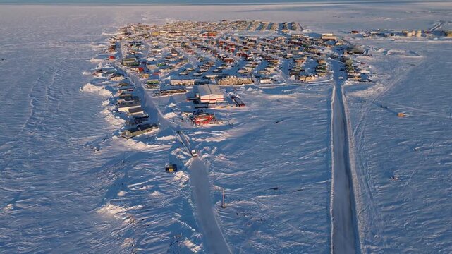 Drone pan up to reveal the horizon then pushes toward Arviat, a remote Arctic community. Shows northern civilization and snowy tundra in winter. Canada North.