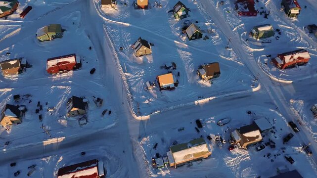 Nadir drone push over Arviat, Nunavut. Colorful houses and long shadows on snow-covered ground at golden hour. Cinematic look at remote northern housing and Arctic urban planning.