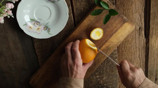 Hands slicing fresh oranges on wooden cutting board. Preparing citrus fruits for mulled wine, lemonade or cocktail. Overhead shot.