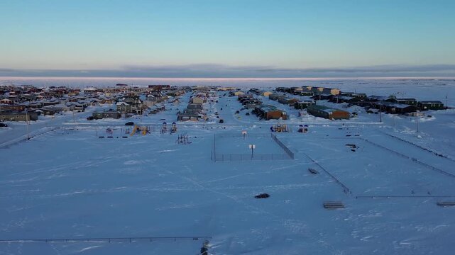Drone push toward a snowy basketball court and playground in Arviat, Nunavut. Shows community infrastructure and recreation in a remote Arctic town during winter.