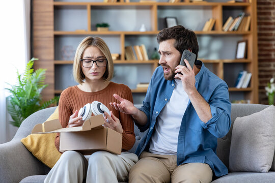 Angry Caucasian man on phone call complaining about broken headphones and delivery scam while woman looks upset. Couple dealing with consumer fraud at home.