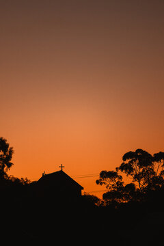 Silhouette of a church with a cross against a vibrant orange sunset sky with copy space