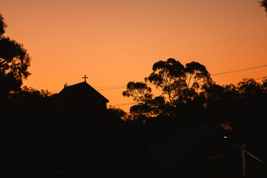 Silhouette of a church with a cross against a vibrant orange sunset sky