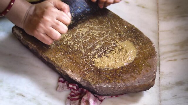 Close up of Indian Woman Hands Grinding Fresh Spices on Traditional Stone Grinder, Manual Food Preparation Using Sil Batta in Indian Kitchen
