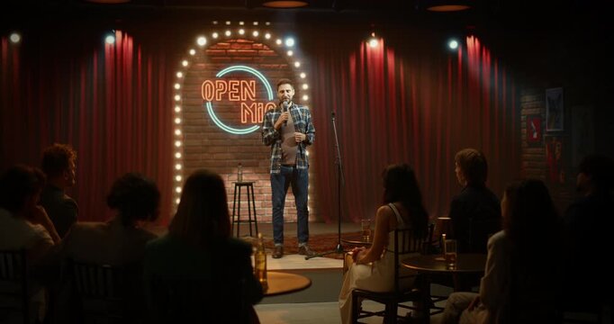 Comedian Performs a Live Stand-up Set at a Bar Open Mic, Riffing Into the Microphone, Checking Notes and Doing Punchlines, Crowd is Laughing Through a Fun Night Stage Show.