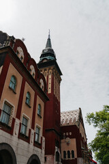 Obraz premium The clock tower and facade of Subotica City Hall rise above the street in Subotica, Serbia. Historic architecture, civic landmark, urban tourism, and European heritage.