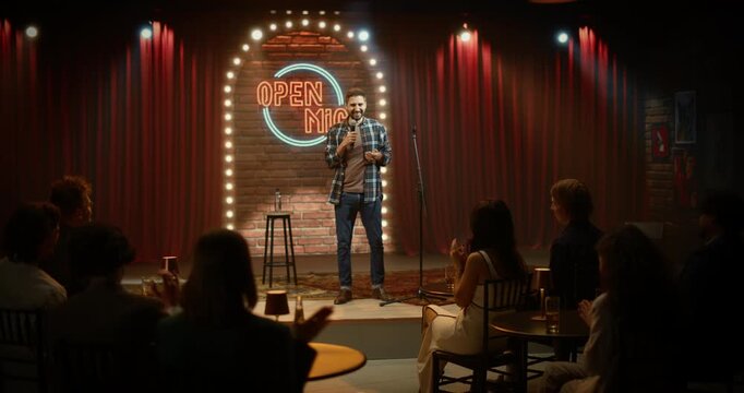 Male Comedian Performs a Live Stand-up Set at an Open Mic Night, Delivering Funny Jokes on Stage in a Cozy Bar Comedy Club as the Audience Laughs, Listens, and Applauds Throughout the Show.