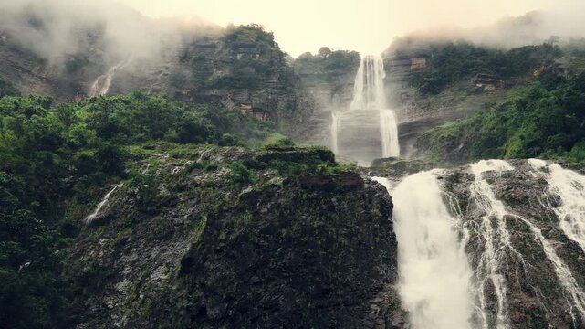 Kynrem Waterfall in Meghalaya India cascading through misty cliffs and lush green forest during monsoon season