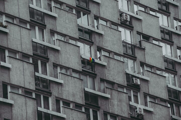 Vibrant LGBTQ rainbow pride flag tied to a balcony's railing of a gray, bleak apartment block, symbolizing diversity and dedicated to pride month © Yurii Zymovin