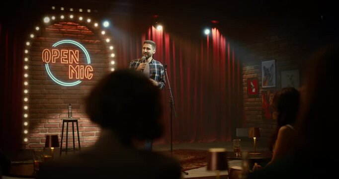 Comedian Delivers a Lively Stand-up Routine at an Open Mic Night, Working the Mic With Sharp Jokes as Bar Customers Laugh and Enjoy the Live Comedy Set on Club Stage Venue.