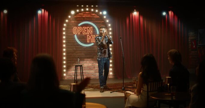 Male Comedian Delivers a Lively Open Mic Stand-up Set on a Small Club Stage, Working the Microphone, Landing Punchlines, and Earning Warm Applause From a Cheerful Bar Audience.