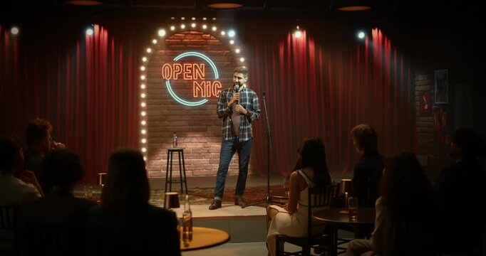 Male Comedian Delivers a Sharp Stand-up Routine at an Open Mic Night, Pacing the Stage With a Handheld Microphone as Bar Patrons Laugh, Listen, and Enjoy the Live Comedy Club Performance.
