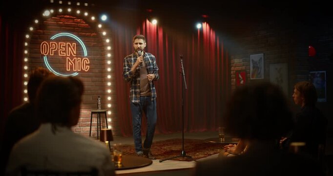 Male Comedian Commands the Comedy Club Stage During an Open Mic Night Performance, Telling Funny Jokes as the Audience Is Having Fun in a Lively Bar Venue Entertainment Show.