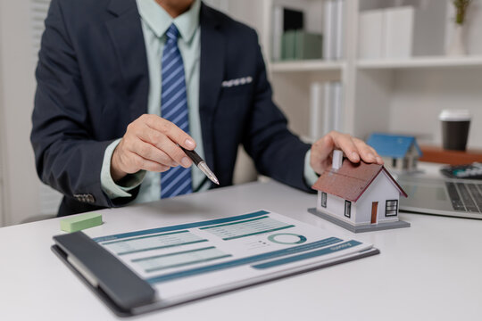 Businessman presenting budget report with property model, explaining financial data, housing cost, and investment planning, representing real estate finance and decision making process.