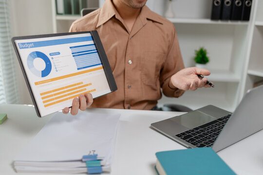 Person presenting budget report on tablet while working with laptop, explaining financial data and expense planning, representing accounting work, finance management, and business decision making.