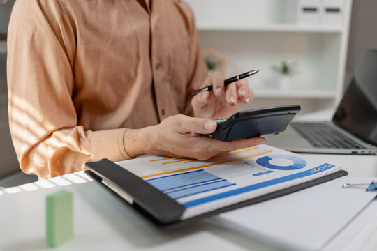 Person using calculator while reviewing budget report on desk, analyzing financial data and expenses, representing accounting work, financial planning, and business management.