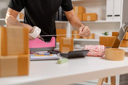 Small business owner tying parcel with string while preparing package for delivery, organizing shipping process and handling ecommerce orders, representing logistics and packaging workflow.