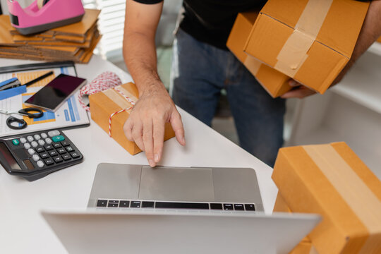 Small business owner preparing multiple parcel boxes while working on laptop, managing shipping orders and packaging workflow, representing ecommerce operations and delivery process.