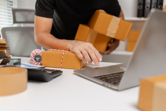 Small business owner preparing multiple parcel boxes while working on laptop, managing shipping orders and packaging workflow, representing ecommerce operations and delivery process.