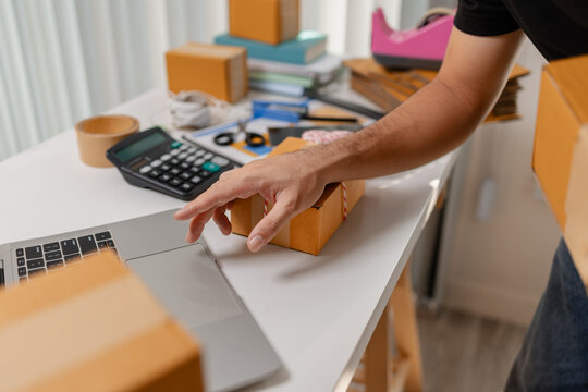 Small business owner preparing multiple parcel boxes while working on laptop, managing shipping orders and packaging workflow, representing ecommerce operations and delivery process.