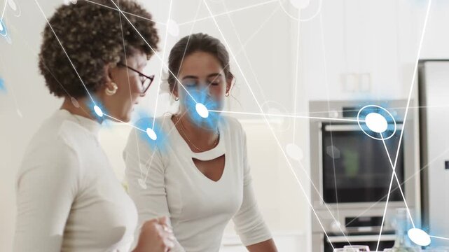 Two women talking at kitchen counter, pointing and starting tech overlay, showing links, hugging