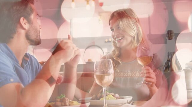 Man gesturing, teasing woman while sharing meal, woman holding wine glass, bokeh flares sweeping