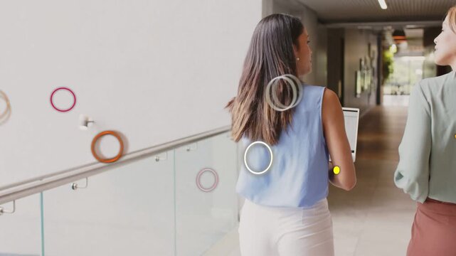 Two female staff walking business hall, gesturing and causing shapes to overlay laptop for work