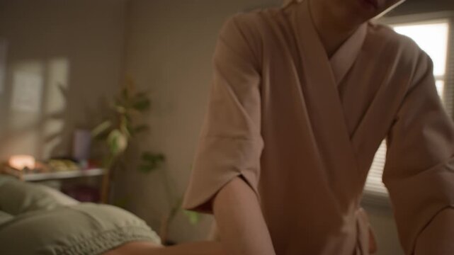 Tilt up of female massage professional performing back massage with oil and strong hands on client during wellness therapy appointment