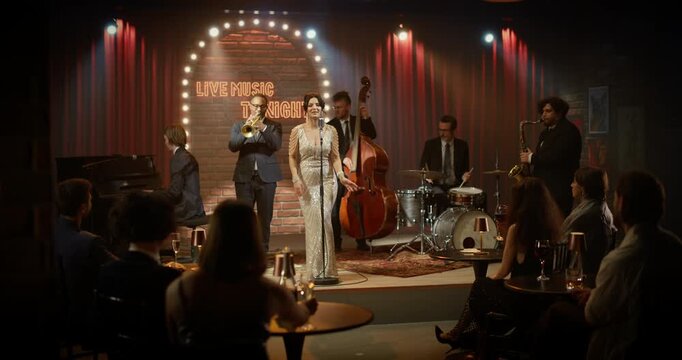 Beautiful Female Singer in a Silver Sequined Gown Sings With a Lively Jazz Combo as Piano, Trumpet, Upright Bass, Drums and Saxophone Animate a Warm Nightclub Concert Before Seated Audience