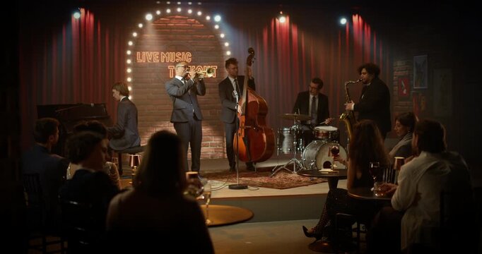 Live Jazz Band Plays Music During a Bar Concert on Stage as a Black Trumpeter Leads Piano, Upright Bass, Drums and Saxophone While the Audience Enjoys Each Song at the Event.