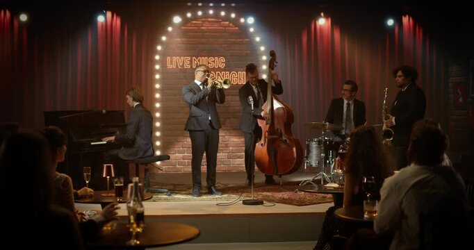 Live Jazz Band Is Playing Music on a Bar Stage During a Concert Event as a Black Trumpeter Leads Piano, Upright Bass, Drums, and Saxophone While the Audience Enjoys Each Song. Wide Shot
