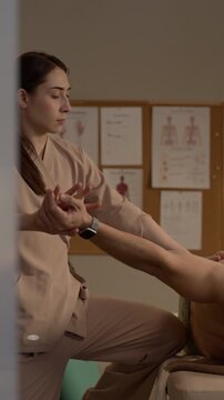 Vertical side view medium shot of female therapist performing shoulder massage using hands in cozy spa environment, showing relaxation and healthcare treatment
