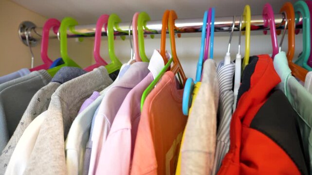Clothes on colorful hangers in the closet. A row of neatly hung casual clothes on colorful plastic hangers in the closet. Bright colors, order and organization of the wardrobe. Children's wardrobe.