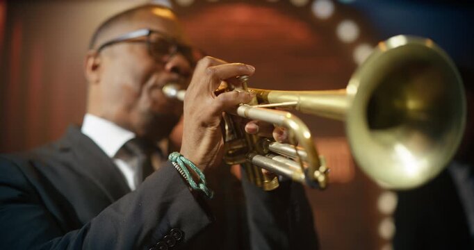 Portrait of Black Male Trumpeter in Glasses Delivers a Blazing Live Jazz Song With His Band on a Bar Stage During a Concert Event, Playing Music for an Energize Audience. Cinematic Close-up