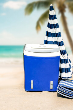 Beach umbrella and portable cooler placed on hot sandy beach under bright sunlight. The scene captures relaxed summer atmosphere with clear blue sky and seaside vibes. Summer and vacation concept.