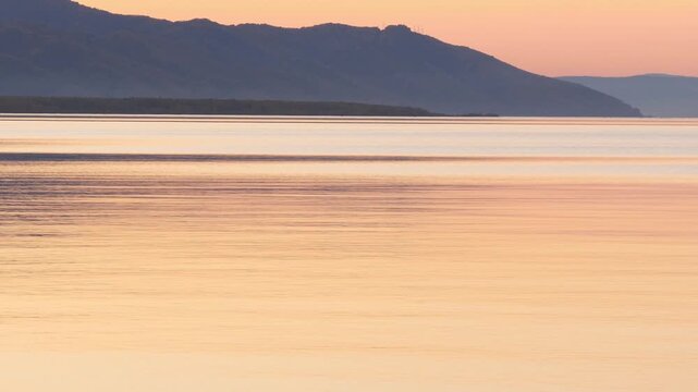 Sunset on Lake Baikal in Russian Siberia on a chilly autumn evening. The orange sky is reflected in the calm surface of the lake.